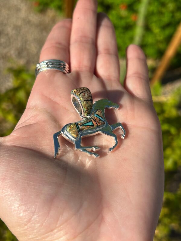 A silver horse pendant with green, blue, and yellow stones.