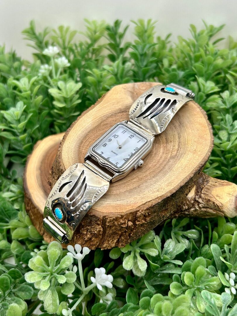 A silver watch with turquoise stones on a piece of wood.