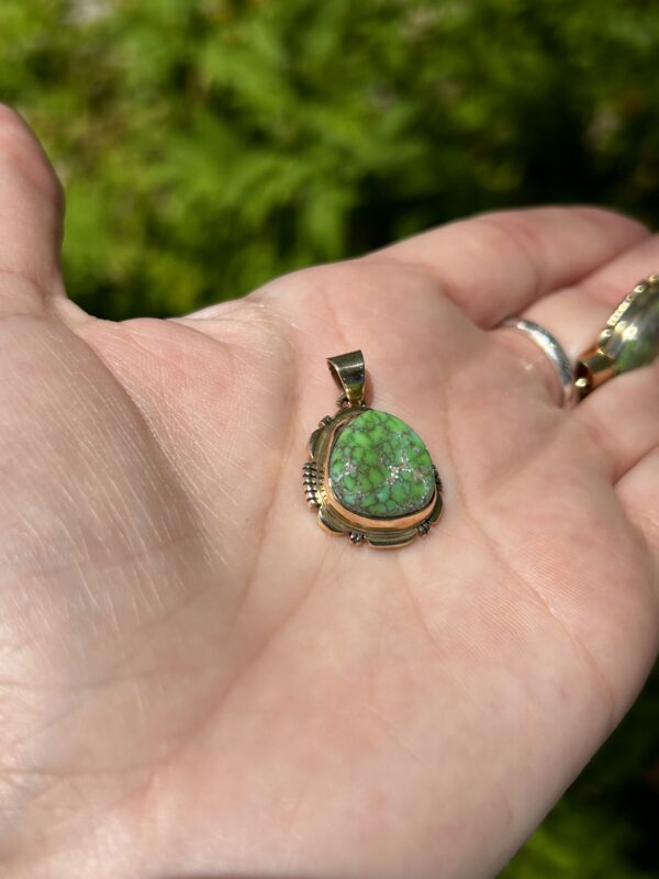 A hand holding a gold pendant with a green stone.