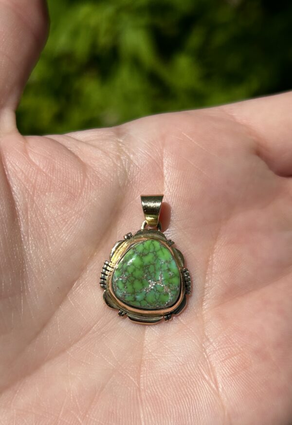 A hand holding a green and gold pendant.