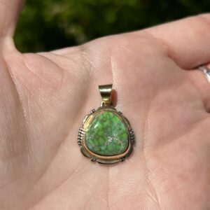 A hand holding a green and gold pendant.