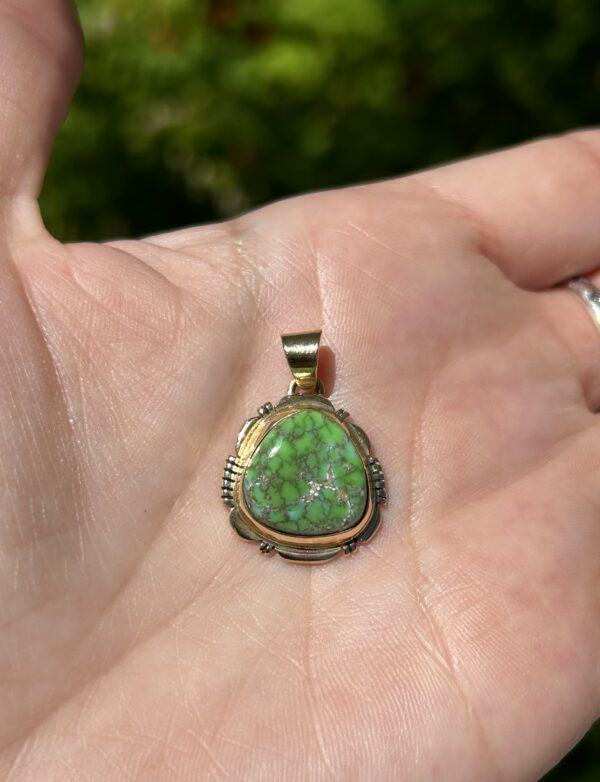 A hand holding a green and gold pendant.