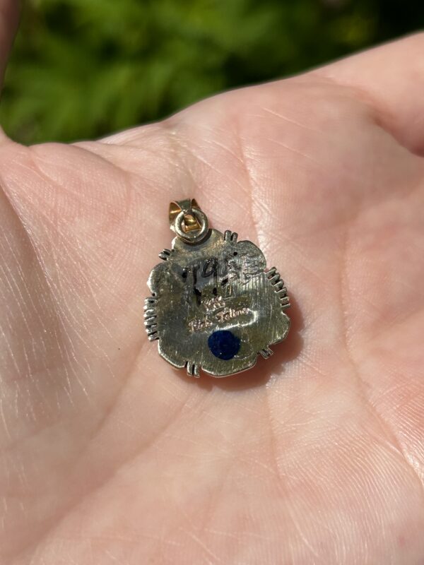 A hand holding a silver and gold pendant.