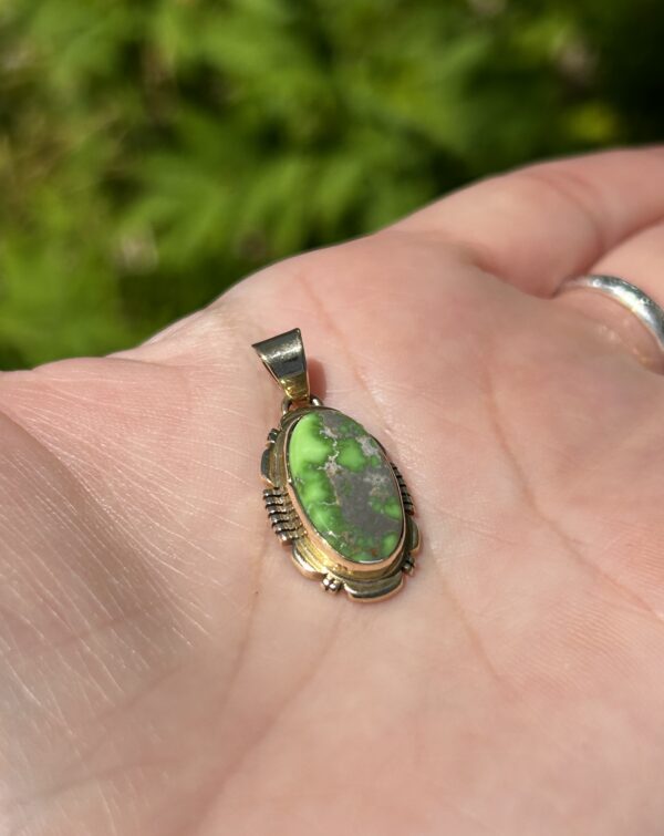 A hand holding an oval green pendant.