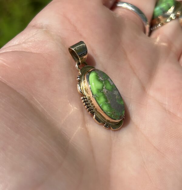 A hand holding an oval green pendant.