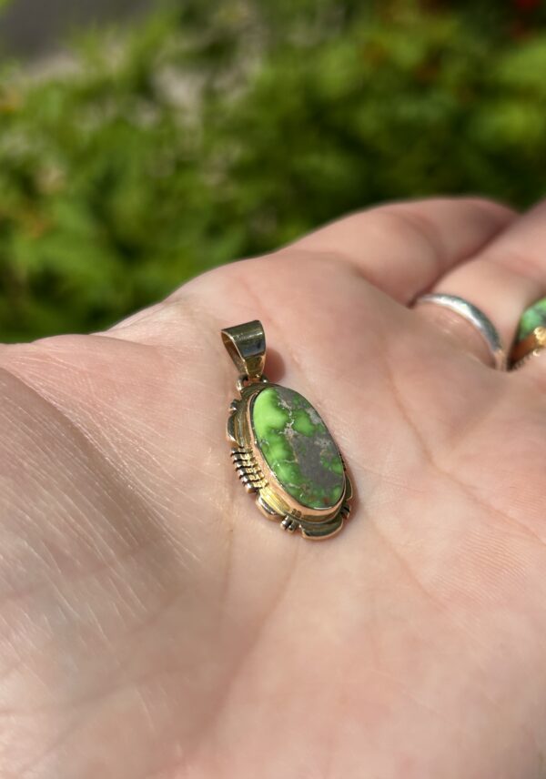 A hand holding a gold pendant with a green stone.