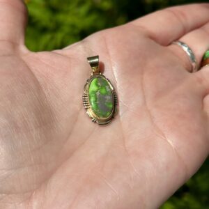 A hand holding an oval green stone pendant.