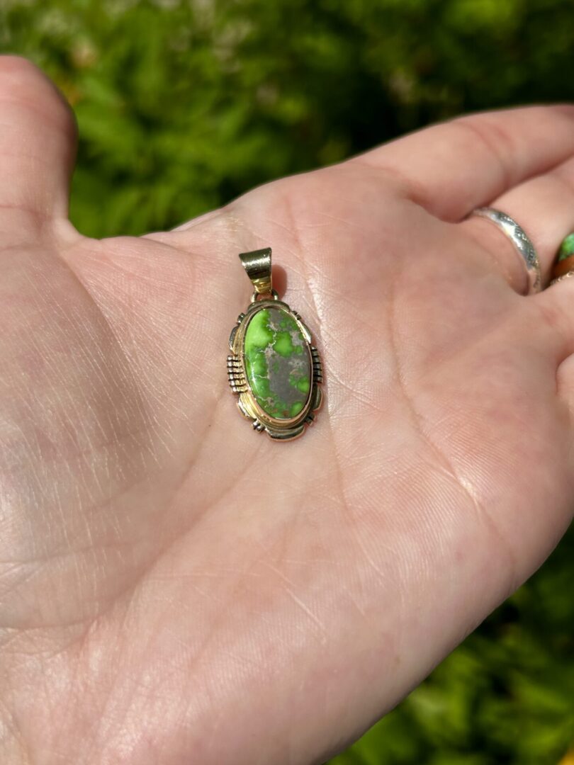 A hand holding an oval green stone pendant.