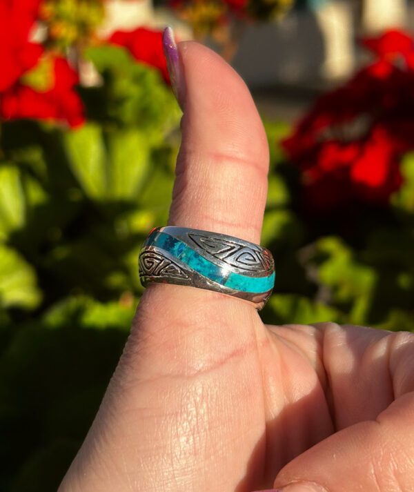 A silver ring with blue stone inlay on a person's thumb.