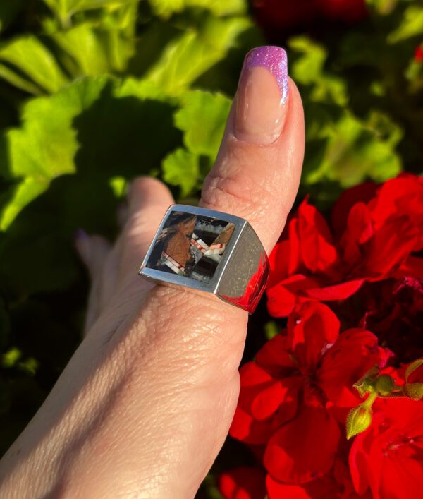 A person wearing a silver ring with a brown stone.