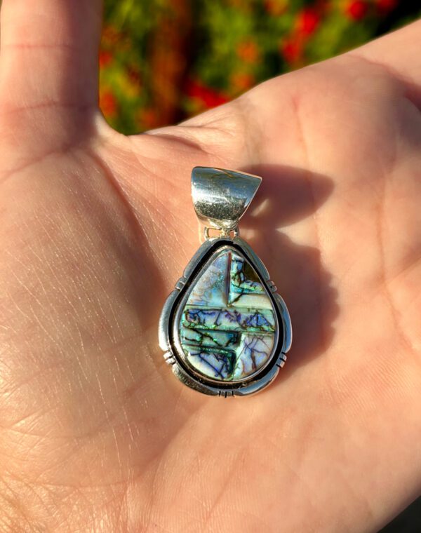 A silver pendant with a colorful stone inlay.