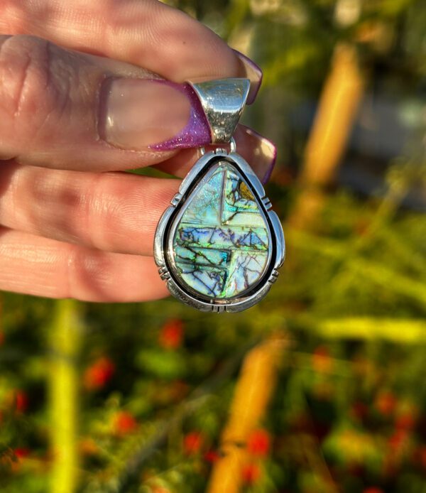 A hand holding a silver pendant with a colorful stone.