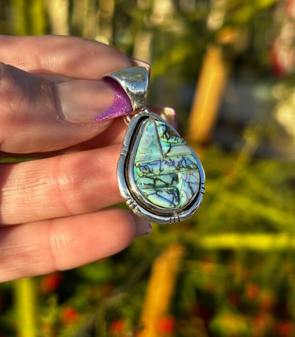 A hand holding a silver pendant with a colorful stone.