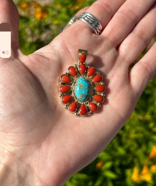 A hand holding a turquoise and coral pendant.