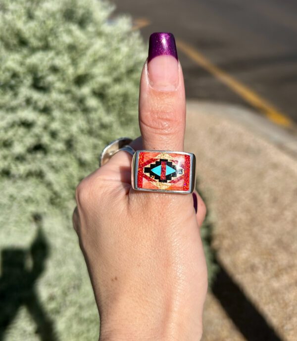 A person wearing a Native American ring with turquoise and coral inlay.