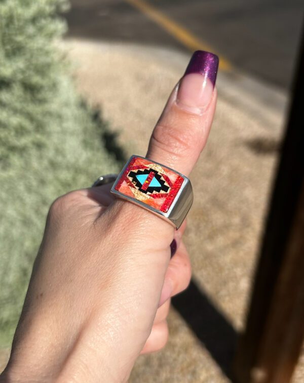 A person wearing a silver ring with red, blue, and green stones.