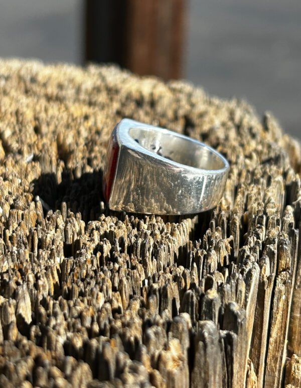 A silver ring with a red stone on a wooden surface.