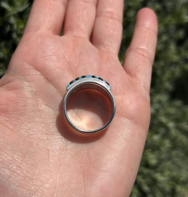 A hand holding a ring with black and white stones.