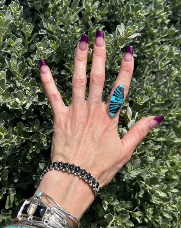 A hand wearing a blue and black ring and beaded bracelets.