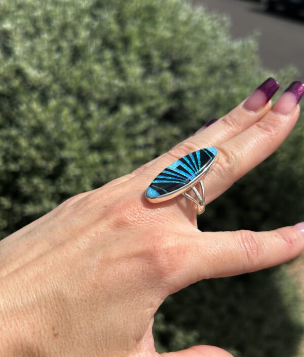 A person is wearing an oval-shaped ring with blue inlay.