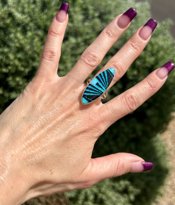 A hand wearing an oval-shaped ring with blue inlay.