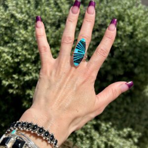 A hand wearing a silver ring with a blue stone.