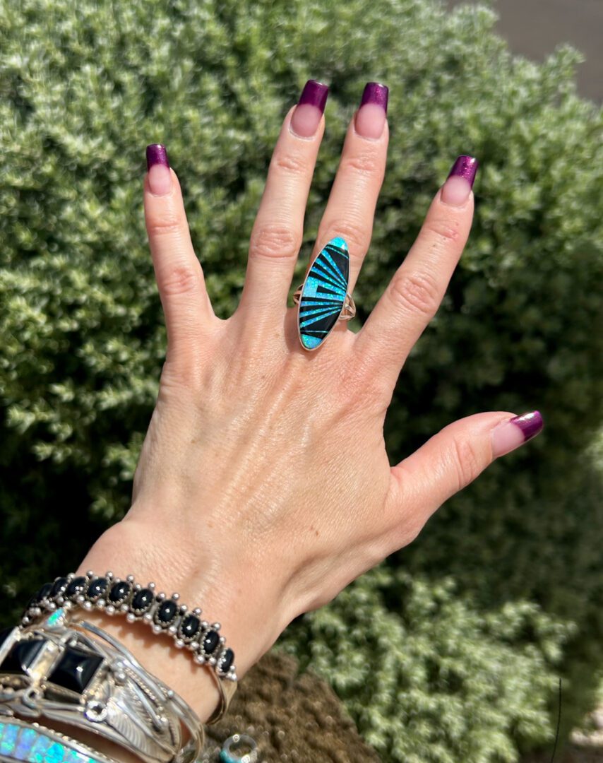 A hand wearing a silver ring with a blue stone.