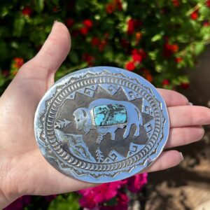 A hand holding a silver and turquoise belt buckle.