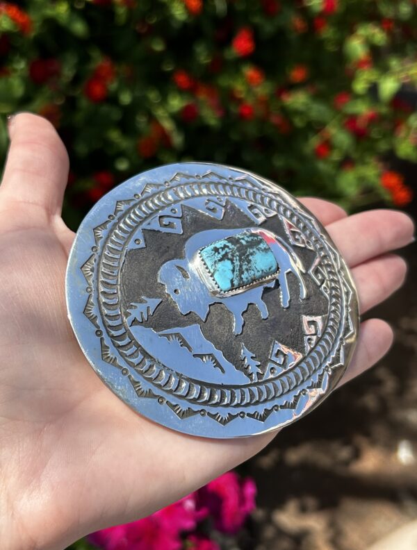 A silver belt buckle with a turquoise stone.