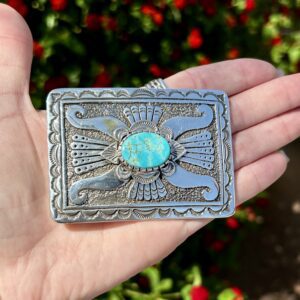 A hand holding a silver and turquoise pendant.