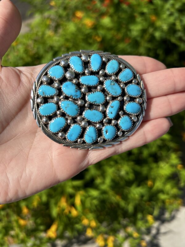 A hand holding a Native American turquoise and silver concha belt buckle.