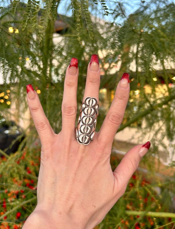 A hand wearing a silver ring with red nails.