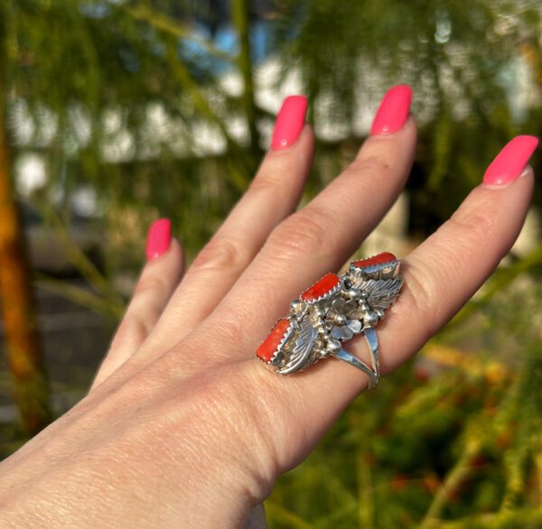 A hand wearing a silver ring with red coral stones.