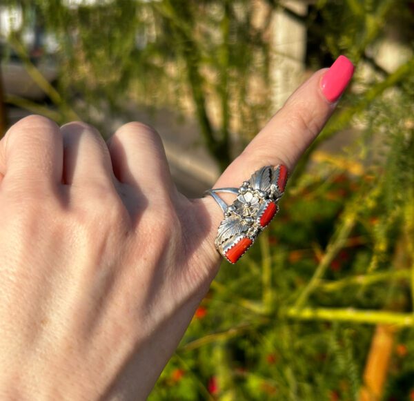 A person is wearing a silver ring with red coral stones.