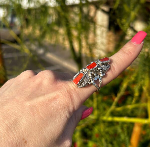 A person is wearing a silver ring with red coral stones.