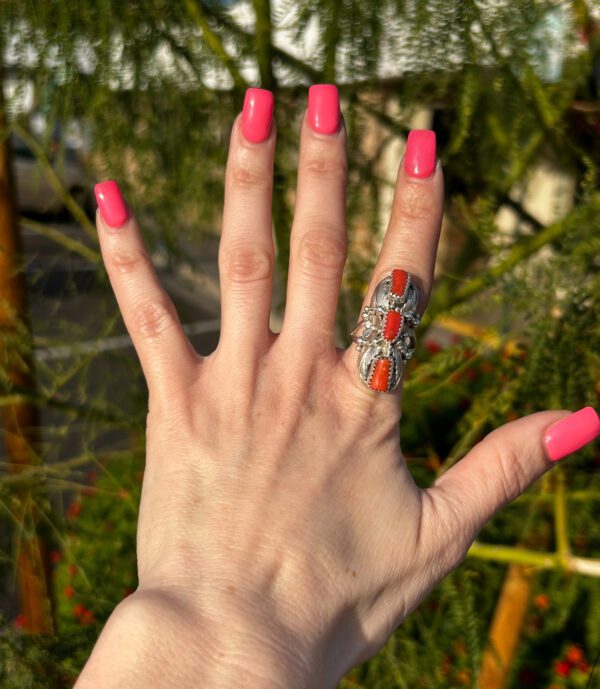 A hand is modeling a silver ring with red coral stones.