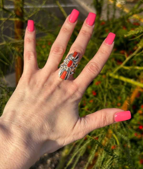 A hand wearing a silver ring with red coral stones.