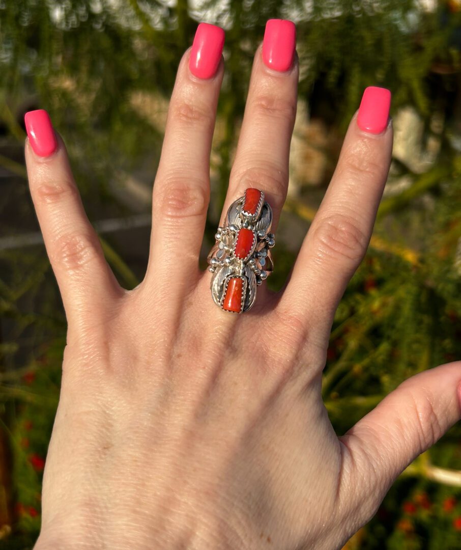 A hand wearing a silver ring with red coral stones.