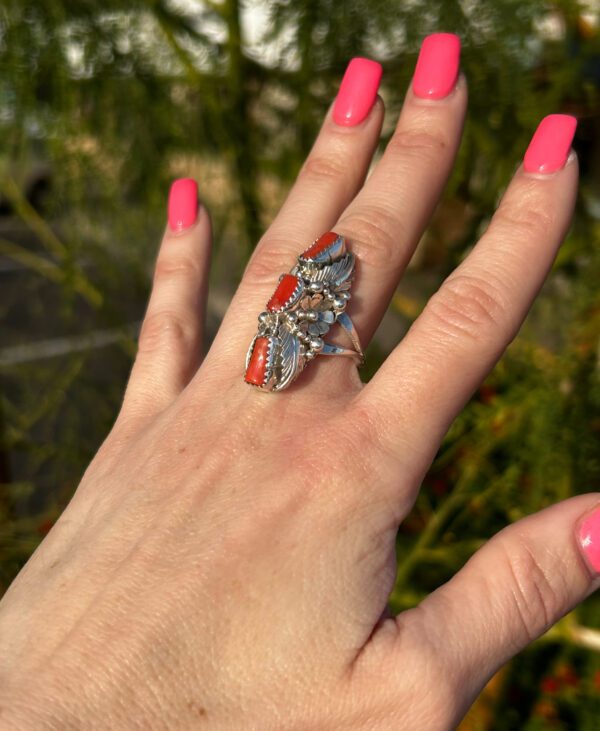 A hand wearing a silver ring with red coral stones.