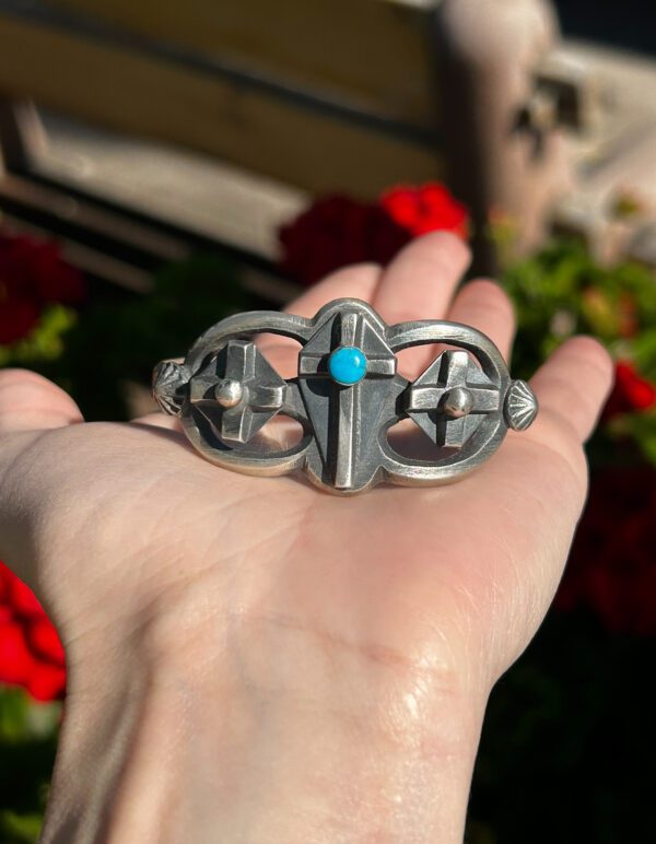 A hand holding a silver and turquoise bracelet.