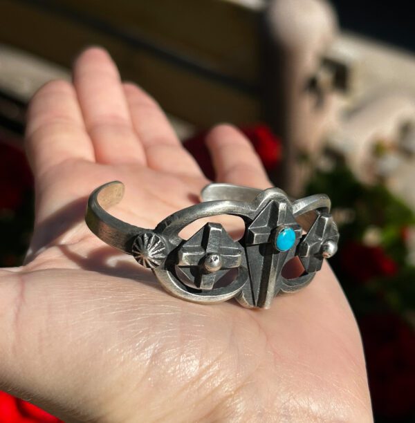 A hand holding a silver and turquoise bracelet.