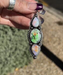 A hand holding a silver pendant with three opal gemstones.