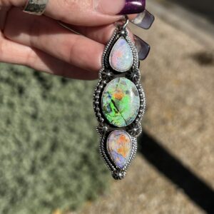 A hand holding a silver pendant with three opal gemstones.