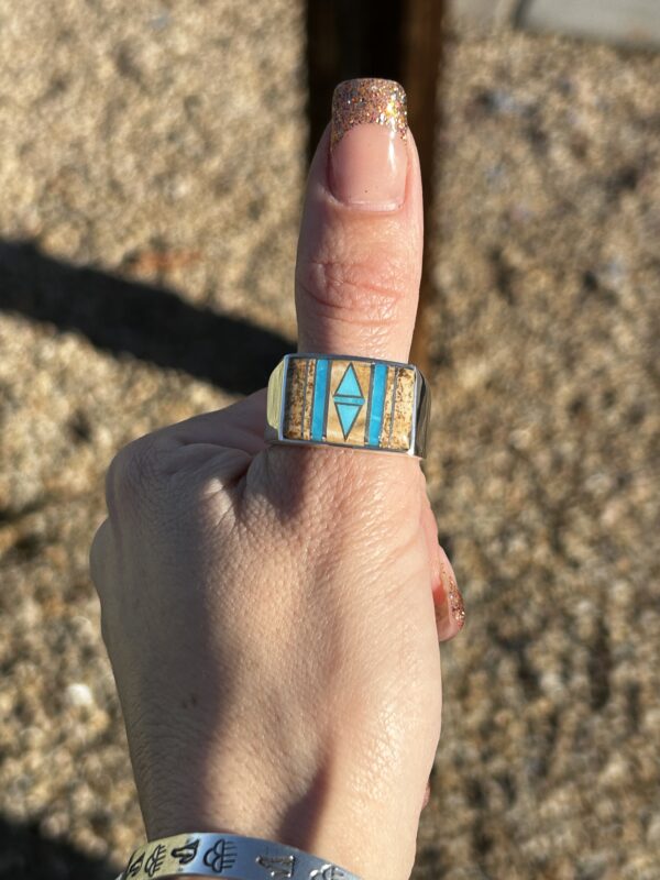 A person wearing a silver ring with turquoise inlay.