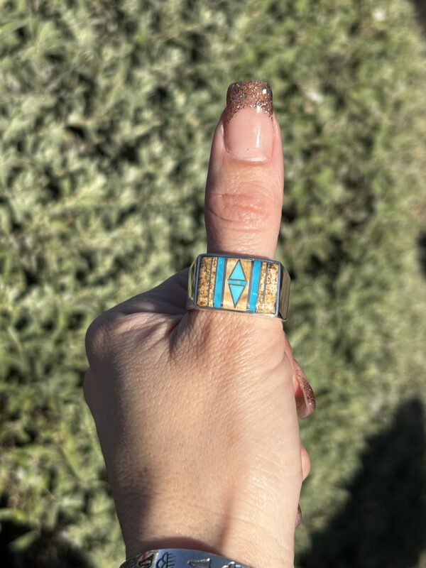 A person wearing a silver ring with turquoise and brown stones.