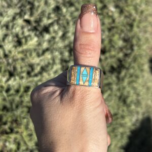 A person wearing a silver ring with turquoise stones.