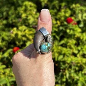 Turquoise and silver claw ring on finger.