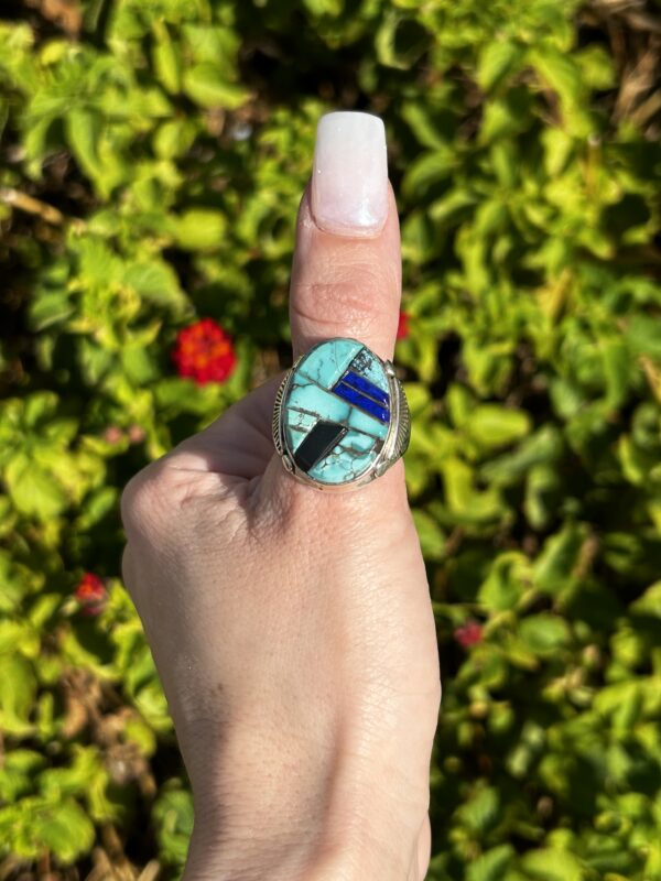 Turquoise and silver inlay ring on finger.