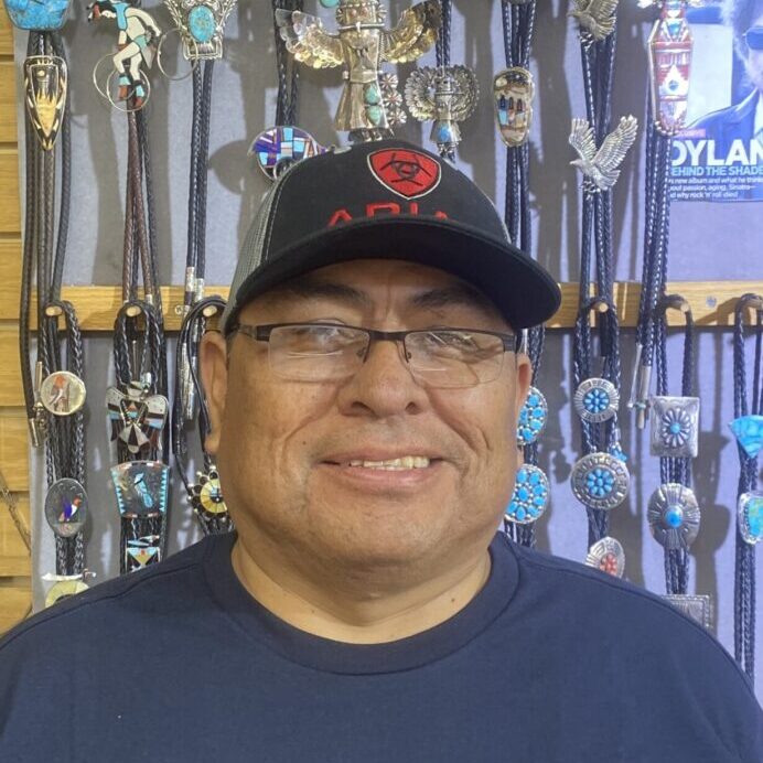 A man wearing glasses and a hat in front of a wall with medals.